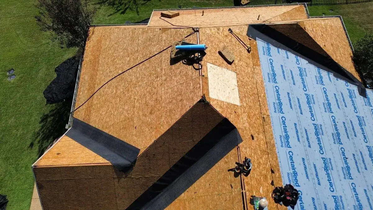 Roof deck stripped to bare sheathing with underlayment rolls staged, seen from above