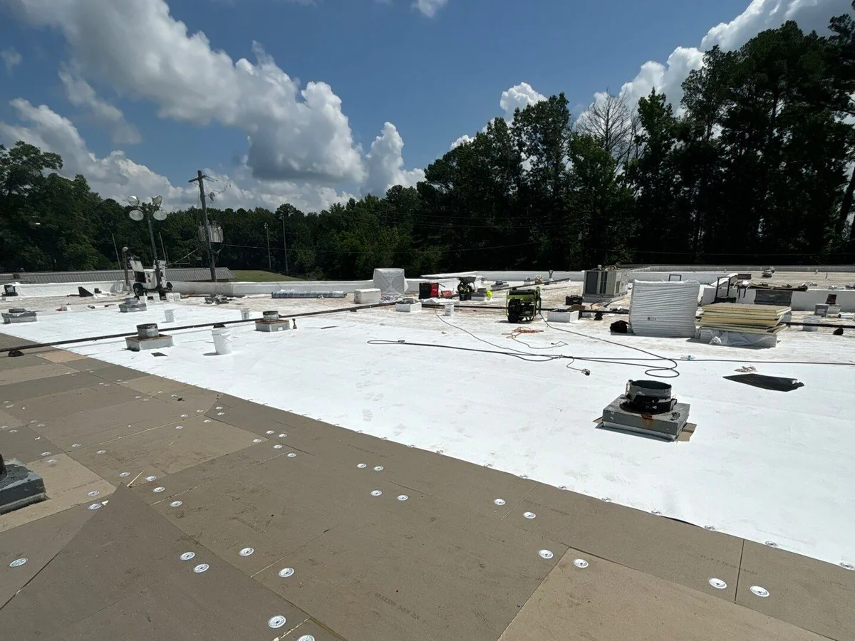 Flat low-slope roof with membrane rolled over cover board, drains and curbs